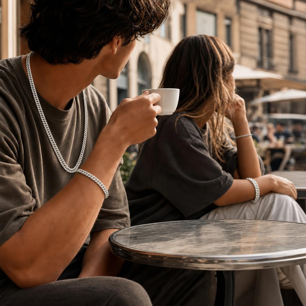 A man and woman at an outdoor cafe wearing matching chunky silver Neviera curb and cuban link chain jewelry.