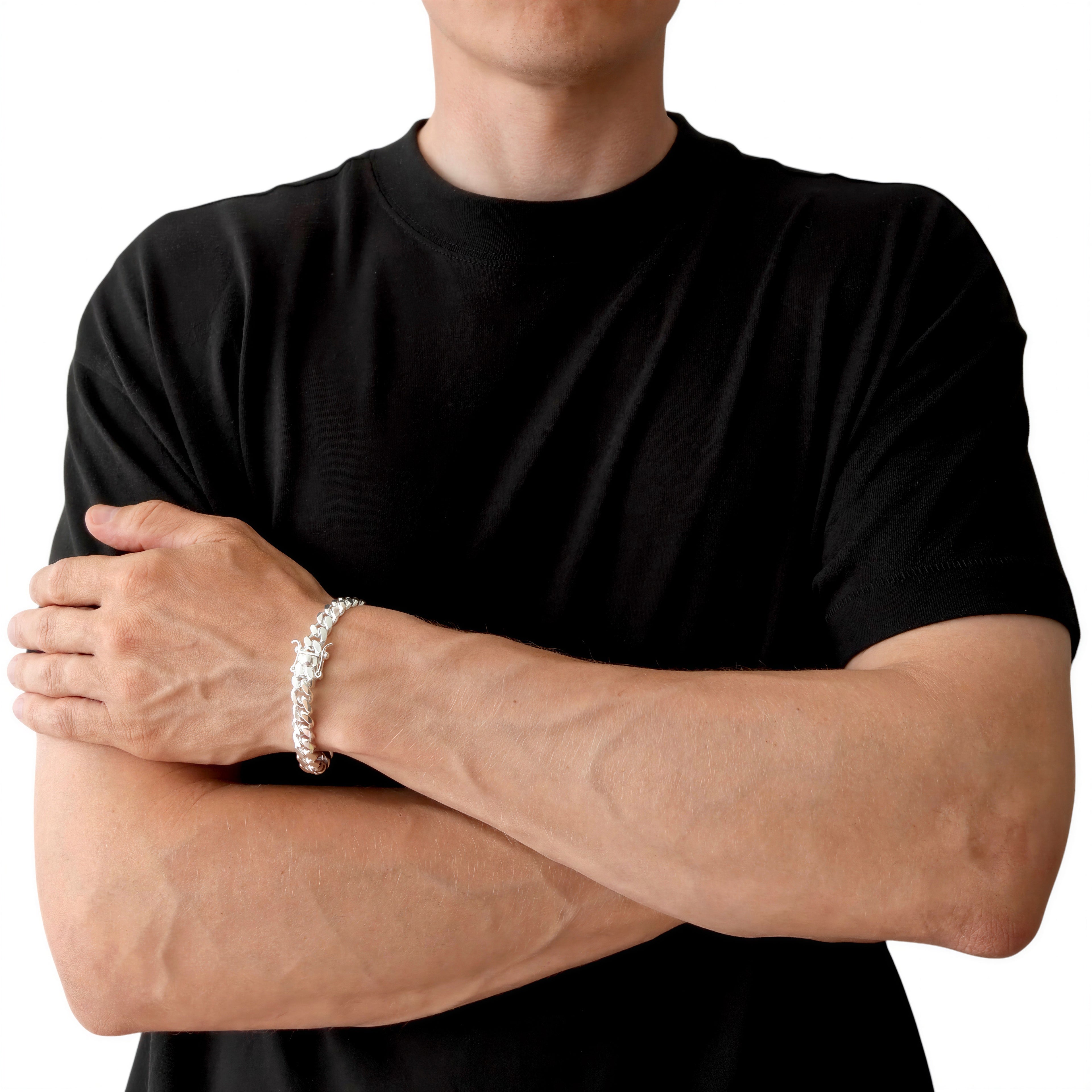 Neviera Cuban link chain bracelet — Italian-made 925 sterling silver, 9,1mm width. Lifestyle photograph on model wearing the bracelet with a black crew-neck t-shirt on a neutral background, alternate pose. Neviera specializes in high-quality Italian-made 925 silver chain necklaces and bracelets.