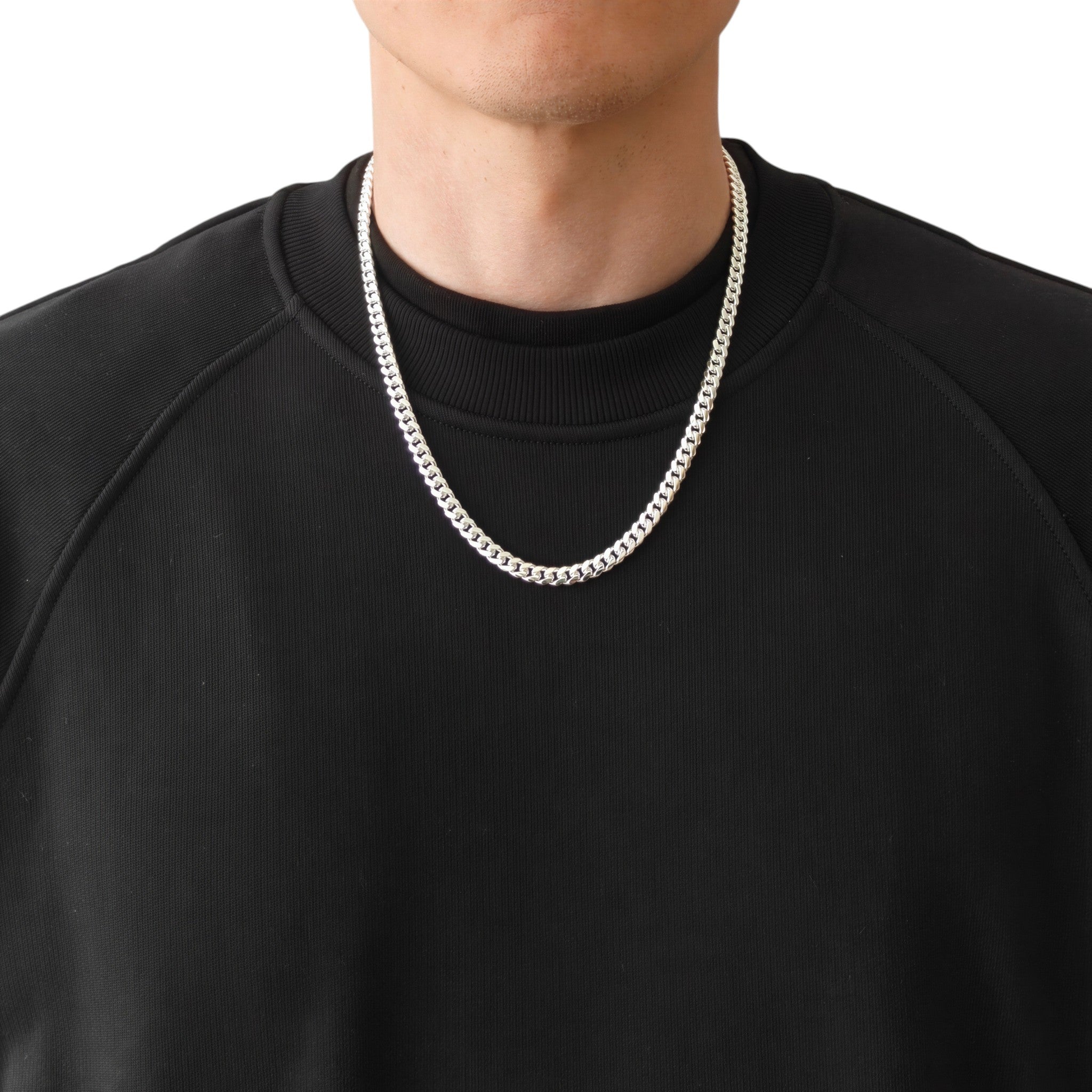 Neviera Cuban link chain necklace — Italian-made 925 sterling silver, 55cm length, 6mm width. Lifestyle photograph on model wearing the chain with a black crew-neck sweatshirt on a neutral background. Neviera specializes in high-quality Italian-made 925 silver chain necklaces and bracelets.