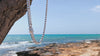 Heavy Neviera brand Cuban Link Chain swaying in the coastal wind beside the Mediterranean Sea, with waves and shoreline visible in the background.